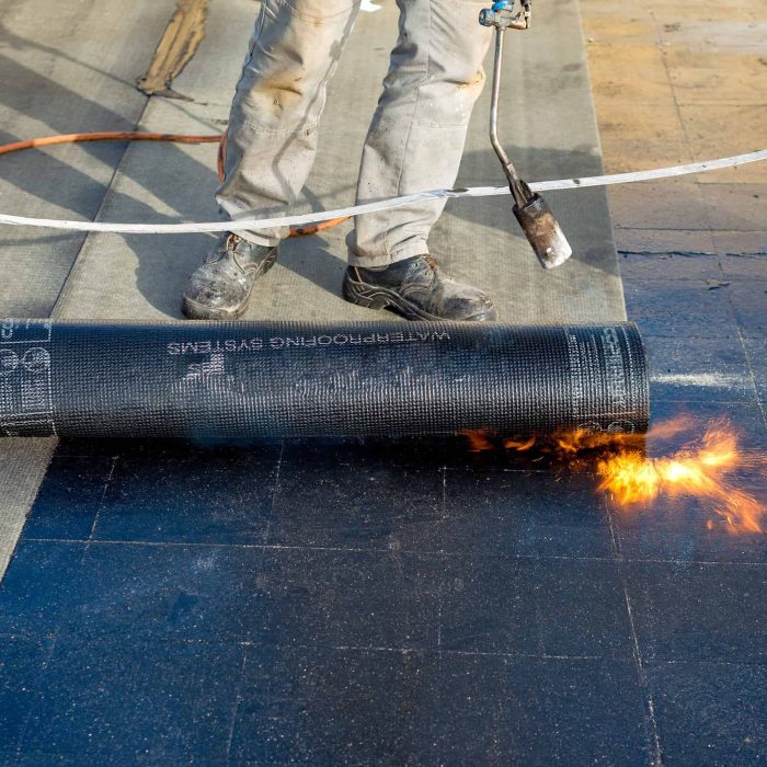 Worker preparing part of bitumen roofing felt roll for melting by gas heater torch flame